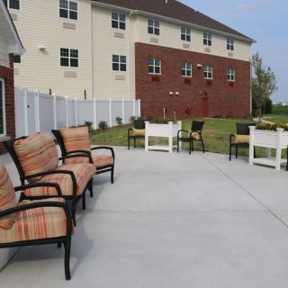An outdoor patio area with chairs and a view of a brick building and fence.
