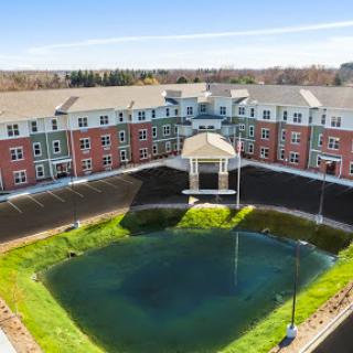 A serene view of a residential building with a central pond and well-maintained lawn.