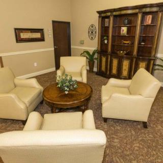 A cozy living room setup featuring four beige armchairs arranged around a round wooden table, with a bookshelf in the background.