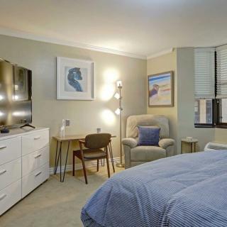 A cozy bedroom with modern decor, featuring a bed, dresser, artwork, and a comfortable chair.