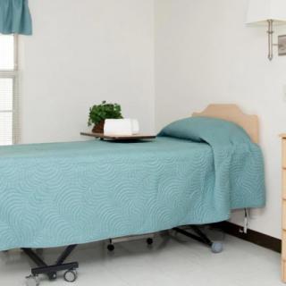 A minimalist hospital room featuring a single bed with light blue bedding.