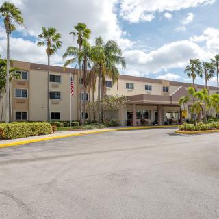 A hotel building with palm trees and a parking lot in front, viewed during the daytime.