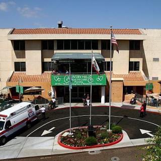 A hospital building with an ambulance parked in front, featuring flags and a main entrance.