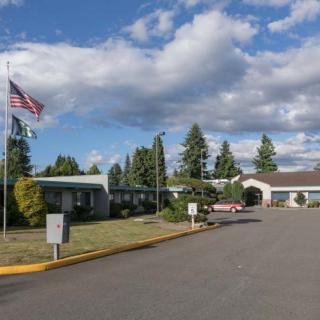 A building with flags and a driveway surrounded by trees under a cloudy sky.