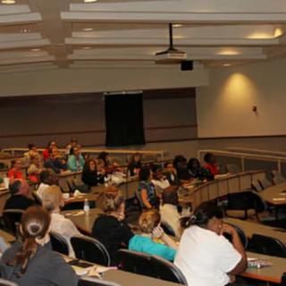 A lecture hall filled with an audience attentively listening to a presentation.