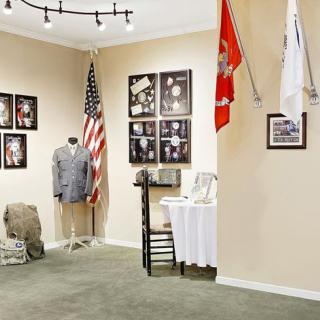 A museum exhibit showcasing military memorabilia, including a uniform and flags, with photographs displayed on the wall.