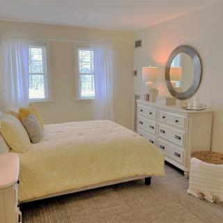 A cozy bedroom with neutral tones, featuring a bed, dresser, and large mirror.