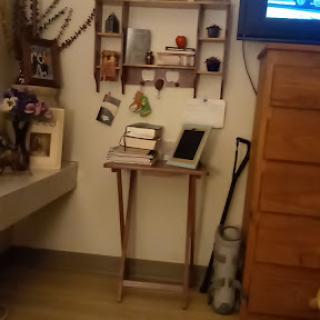 A cozy corner featuring a wooden shelf with various decorations, books, and a tablet on a small table.
