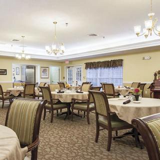 A spacious dining room with elegantly set tables and upholstered chairs, illuminated by chandeliers.