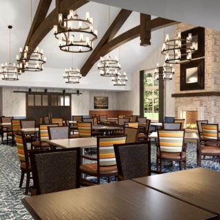 A spacious dining room with wooden furniture, chandeliers, and a large fireplace.