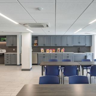 A modern office kitchen with blue chairs and spacious gray cabinets.