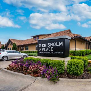 A healthcare facility named Chisholm Place, featuring well-maintained landscaping and a clear sky overhead.