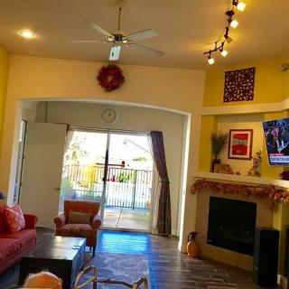 A cozy living room featuring a fireplace, ceiling fan, and a television, with natural light streaming through the window.