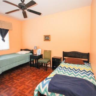 A cozy bedroom with two twin beds, featuring orange walls and a wooden floor, complemented by a ceiling fan.