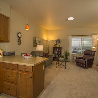A cozy living room with a view of the kitchen area, featuring comfortable seating and warm lighting.