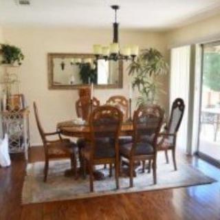 A warm and inviting dining room featuring a wooden table set with matching chairs, complemented by a patterned rug and lush plants. Natural light pours in through the sliding glass door, highlighting the elegant decor.