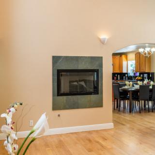 A modern open-concept living space featuring a sleek fireplace, wood flooring, and a glimpse into the dining area.