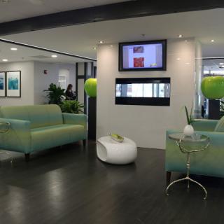 A modern lobby with green couches and decorative plants, featuring a wall-mounted television.