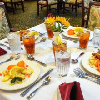 A beautifully set dining table with plates of food and glasses of iced tea.