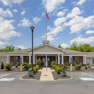 A front view of a symmetrical building with a flagpole and well-maintained landscaping under a partly cloudy sky.