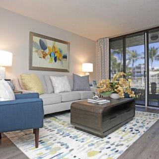 A cozy and modern living room with stylish furniture, featuring a sofa and blue armchair, complemented by a decorative rug and artwork. Large windows offer a view of the outdoors.