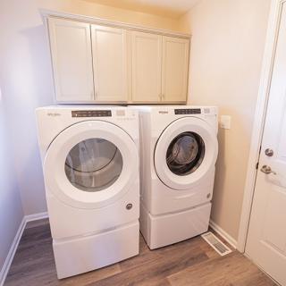 A laundry room featuring a front-loading washer and dryer set beneath overhead cabinets.