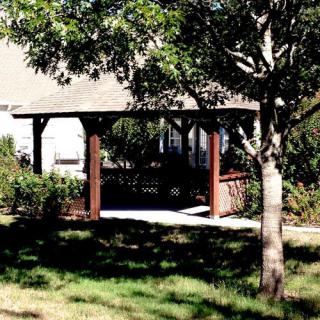 A wooden gazebo providing shade in a sunny garden area.