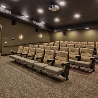 An empty theater room with rows of seats and a ceiling-mounted projector.