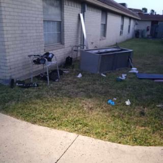 A yard with scattered debris and a large plastic container beside a building.