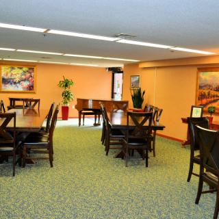 A well-lit dining area with multiple tables and chairs, decorated with paintings and a piano.