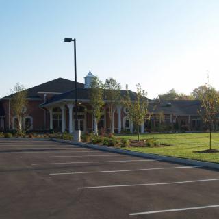 A large building with a parking lot, surrounded by trees on a sunny day.