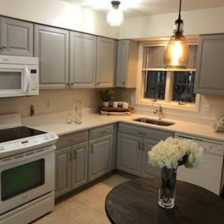 A cozy kitchen featuring gray cabinets, white appliances, and modern lighting with a vase of flowers on the table.