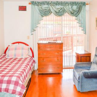 A cozy bedroom with a single plaid-bedded frame, dresser, and comfortable armchair next to a window with curtains.