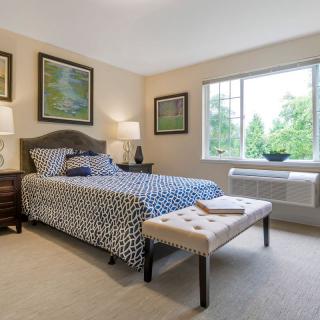 A cozy bedroom with a patterned bedspread, framed artwork, and a large window letting in natural light.