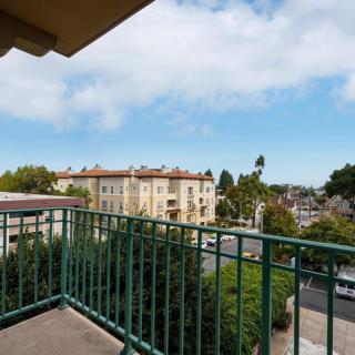 A balcony overlooking an urban scene with buildings and trees under a cloudy sky.