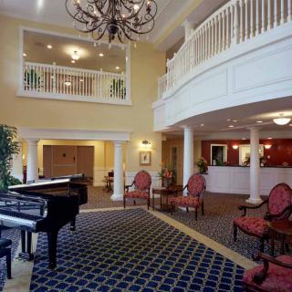 A spacious hotel lobby featuring a grand piano and elegant seating area under a chandelier.