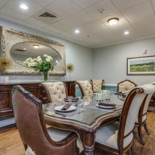 An elegantly decorated dining room featuring luxurious furniture, a sophisticated table setting, and decorative elements like a large mirror and flower arrangement.