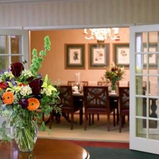 A beautifully arranged bouquet of flowers in a vase, placed near an elegantly set dining room with open double doors.