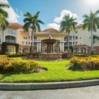 A luxurious residential building with a central fountain, surrounded by well-maintained landscaping and palm trees under a sunny sky.