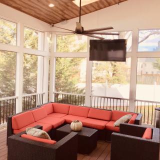 A modern sunroom with comfortable red-cushioned seating, a ceiling fan, and a mounted TV.