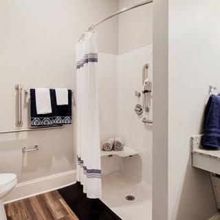 A modern bathroom with an accessible shower featuring white walls, a curtain, and neatly arranged towels.
