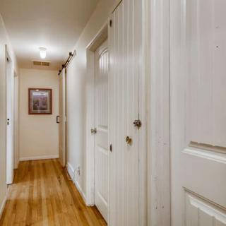 A well-lit hallway with wooden floors and several doors.
