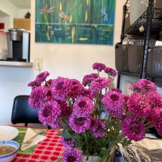 A vase of vibrant purple flowers on a table in a cozy interior setting.