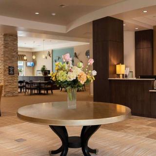 A modern hotel lobby featuring a round table with a floral arrangement and a reception desk.