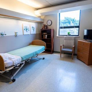 A clean and well-organized hospital room featuring a bed, chair, and natural light from the window.