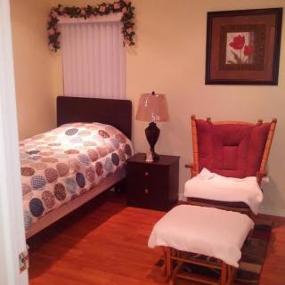 A cozy bedroom with a bed, nightstand, lamp, and a cushioned chair with a footrest.