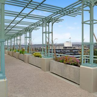 A pergola-covered walkway with views of the city and surrounding landscape.