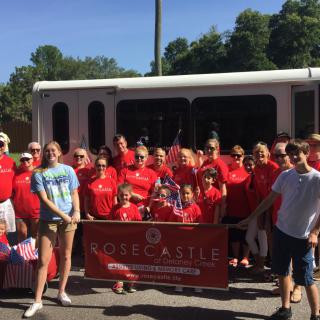 A group of people in red shirts pose with a banner outdoors, possibly as part of a parade or team event.