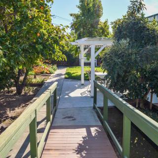 A sunny garden pathway featuring a small wooden bridge surrounded by lush greenery.