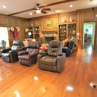 A cozy living room with several recliner chairs, wood paneling, a fireplace, and decorative shelves.
